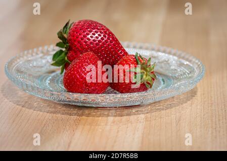 Fraises rouges fraîches sur une assiette en verre décorative transparente. La plaque ronde est assise sur une table en bois de chêne. Banque D'Images