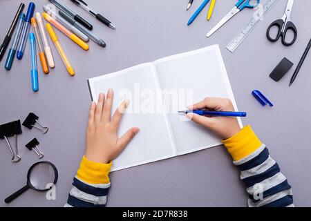 Concept d'éducation. Un stylo dans les mains d'un garçon, un carnet à carreaux ouvert et divers articles de papeterie. Banque D'Images