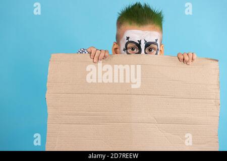 Enfant découragé tenant un carton vierge de protestation avec de l'espace libre isolé sur fond bleu. Fêtez Halloween Banque D'Images