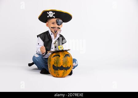 Garçon avec un sourire mignon portant un chapeau de pirate. À proximité se trouve une citrouille dans un chapeau noir fait à la main. Poser pour la caméra. Banque D'Images