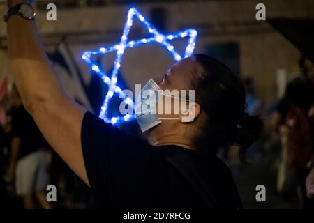 JÉRUSALEM, ISRAËL - OCTOBRE 24 : un manifestant portant un masque protecteur en raison de la pandémie du coronavirus COVID-19 tient une étoile illuminée de David lors d'une manifestation de masse devant la résidence officielle du premier ministre le 24 octobre 2020 à Jérusalem, en Israël. Les organisateurs de la manifestation ont déclaré dans une déclaration que 170,000 personnes se sont montrées pour manifester contre le Premier ministre Benjamin de tout le pays exigeant sa démission en raison de son inculpation pour corruption et pour la gestion de la pandémie COVID-19. Banque D'Images