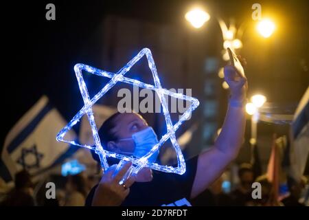 JÉRUSALEM, ISRAËL - OCTOBRE 24 : un manifestant portant un masque protecteur en raison de la pandémie du coronavirus COVID-19 prend un selfie alors qu'elle tient une étoile de David illuminée lors d'une manifestation de masse devant la résidence officielle du premier ministre le 24 octobre 2020 à Jérusalem, en Israël. Les organisateurs de la manifestation ont déclaré dans une déclaration que 170,000 personnes se sont montrées pour manifester contre le Premier ministre Benjamin de tout le pays exigeant sa démission en raison de son inculpation pour corruption et pour la gestion de la pandémie COVID-19. Banque D'Images