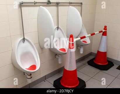 Cônes de circulation orange dans les toilettes publiques des hommes et Urinoirs non utilisés pour la distanciation sociale due à Covid 19 épidémie pandémique en Irlande Banque D'Images