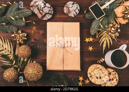 Boîte cadeau de Noël faite à la main, en papier artisanal, avec décorations dorées, branches de sapin, biscuits et tasse à café, plat. Banque D'Images