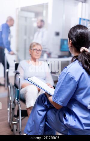 Une infirmière parle de son incapacité avec une femme handicapée en fauteuil roulant. Aide pour les personnes handicapées. Assistance pour les personnes âgées avec cadre de marche. Banque D'Images