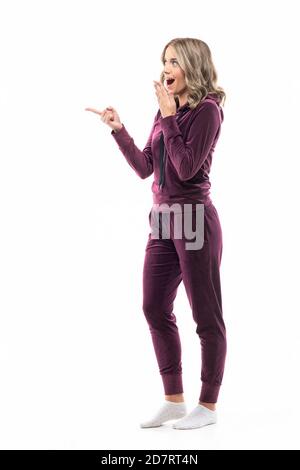 Une jeune femme stupéfaite qui se met à remarquer l'espace de copie dans les vêtements de la maison. Concept de remise shopping. Pleine longueur isolée sur fond blanc. Banque D'Images