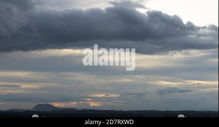 Une silhouette panoramique de collines dans le fond avec foncé nuages à l'horizon avec le soleil qui les traverse Banque D'Images