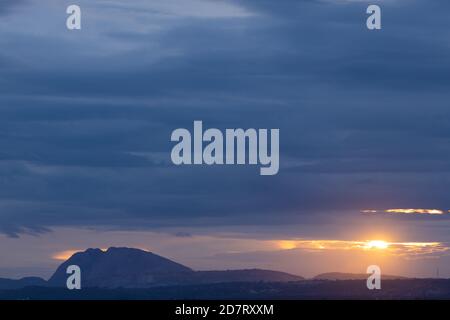 Une silhouette panoramique de collines dans le fond avec foncé nuages à l'horizon avec le soleil qui les traverse Banque D'Images