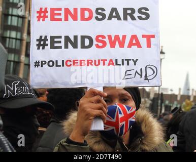 Un manifestant portant un masque facial tient une bannière demandant de mettre fin au SRAS et à la brutalité policière au Nigeria.des Nigérians basés à Londres protestent sur la place du Parlement contre la brutalité de la Squad spécial anti-vol (SRAS) de la police nigériane. Amnesty International a confirmé qu'elle avait des preuves d'un usage excessif de la force ayant entraîné la mort de manifestants à la porte de péage de Lekki mardi dernier. Le Président Buhari a dissous le SRAS le 11 octobre, mais ces manifestants ont toujours appelé à sa démission. Banque D'Images