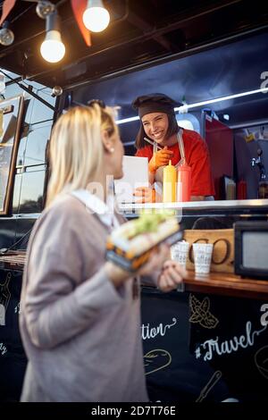 image verticale d'un client avec un sandwich entre les mains, parlant à un employé d'un service de restauration rapide, souriant Banque D'Images