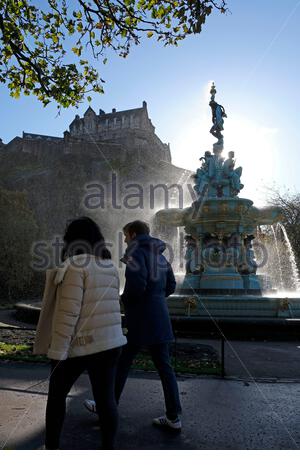 Édimbourg, Écosse, Royaume-Uni. 25 octobre 2020. Vents violents créant beaucoup de jets sur la fontaine Ross, normalement tranquille, des jardins de West Princes Street, les piétons prenant soin de ne pas se mouiller. Le soleil rétro-éclairé et filtrant à travers le spray, avec une vue sur le château d'Édimbourg. Crédit : Craig Brown/Alay Live News Banque D'Images