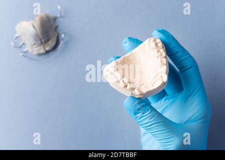 main du dentiste dans un gant bleu tenant une fonte de plâtre pour enfants mâchoire sur fond bleu Banque D'Images