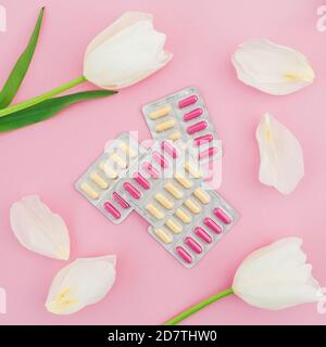 Concept médical avec des pilules de vitamines et des fleurs blanches sur fond rose. Flat lay, vue de dessus. Banque D'Images