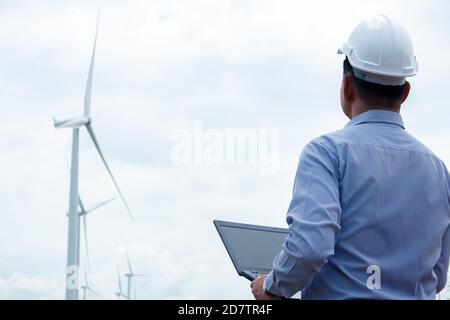 Les ingénieurs des moulins à vent travaillent sur ordinateur portable avec l'éolienne en arrière-plan Banque D'Images