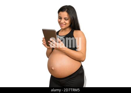 Portrait d'une femme enceinte latine utilisant une tablette numérique sur fond blanc. La maternité et la grossesse concept. Banque D'Images