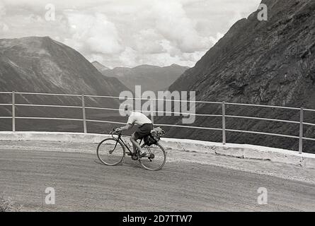 Années 1950, historique, cycliste de tourisme sur une route de pont de gravier dans les Alpes suisses. Banque D'Images