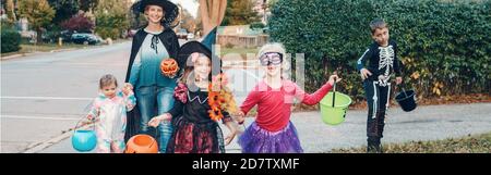 Trick or Treat. Mère avec des enfants qui vont jouer ou se gâter à Halloween. Maman avec des enfants en costumes de fête avec des paniers allant aux maisons de quartier Banque D'Images