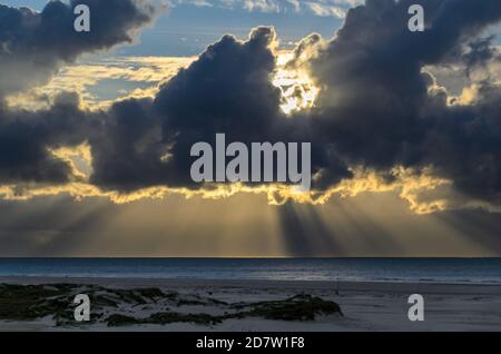 Île d'Amrum, Allemagne : rayons du soleil émergeant à travers les nuages sombres de la tempête sur la plage d'Amrum. Le coucher du soleil est masqué par un front de nuage épais annonçant mauvais Banque D'Images