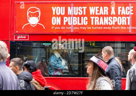 Les manifestants défilent devant une femme portant un masque sur un bus portant une signalisation COVID-19 lors d'un rassemblement anti-verrouillage à Londres, le 24 octobre 2020 Banque D'Images