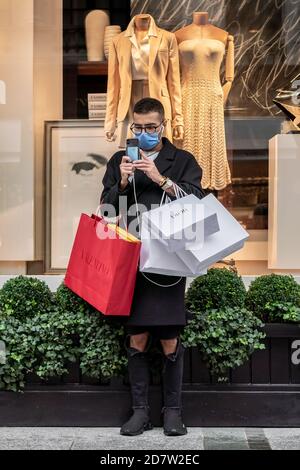 Londres, Royaume-Uni. 25 octobre 2020. Coronavirus : sur Savile Row, un client masqué vérifie son téléphone tenant des sacs d'achats de luxe lors d'un dimanche après-midi humide. Credit: Guy Corbishley/Alamy Live News Banque D'Images