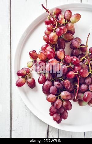 Raisins rouges mûrs dans une assiette sur fond de bois blanc. Vue de dessus. Banque D'Images