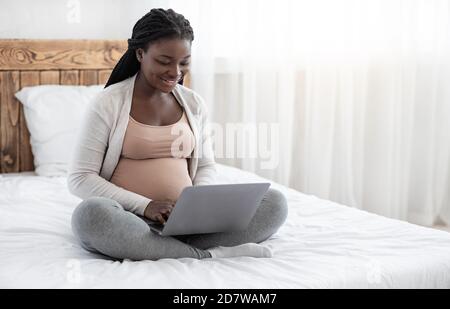 Femme enceinte noire utilisant un ordinateur portable à la maison, travaillant à distance ou magasiner en ligne Banque D'Images