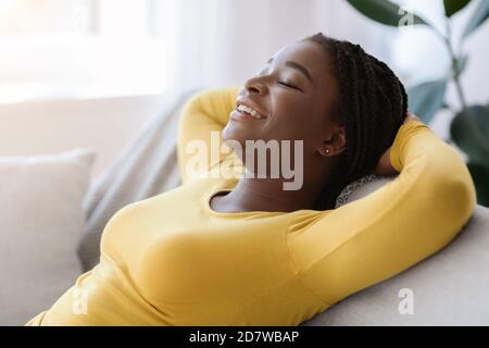 Détente à l'intérieur. Une dame noire souriante se penchée sur le canapé avec les yeux fermés Banque D'Images