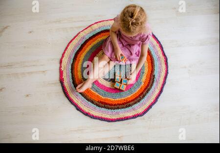 un jeune enfant de 4 ans s'assoit sur un crochet rond coloré Tapis de fils de T-shirts réaffectés sur un plancher laminé blanc et jouez les cubes de bois naturel avec la laisse Banque D'Images