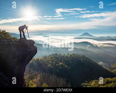 Photographe cadrage de la scène dans le viseur. L'homme utilise l'appareil photo sur trépied pour prendre des photos de paysages de montagnes brumeuses. Détendez-vous sur le concept de vacances Banque D'Images