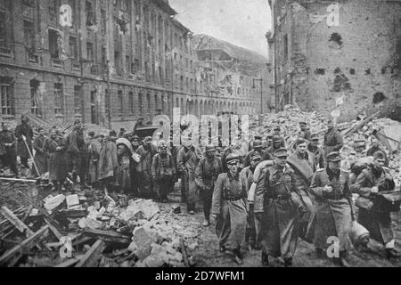 BERLIN 1945. Légende originale : « après que Berlin s'est finalement rendu à l'Armée rouge à 15:00 le 2 mai 1945, des colonnes de prisonniers allemands, dont beaucoup étaient à moitié avides de l'épreuve par laquelle ils étaient venus, ont commencé à être entamées dans des camps de prison à la périphérie de la ville. Beaucoup ont ri hystériquement et ne pouvaient pas arrêter de rire pendant qu'ils ont traîné à travers la ville brisée. Ici, quelques-uns des 120,000 prisonniers pris en huit jours de combat pour la capitale sortent d'un bâtiment en ruines sur le chemin de la captivité. Banque D'Images