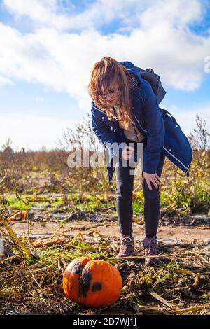 Une jeune femme piquant une citrouille inspectant une citrouille sous un ciel bleu, prête pour Halloween. Banque D'Images