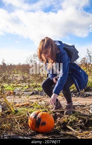 Une jeune femme piquant une citrouille inspectant une citrouille sous un ciel bleu, prête pour Halloween. Banque D'Images