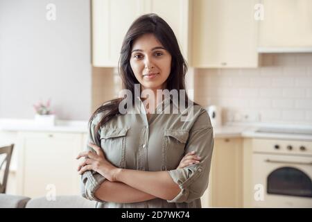 Jeune femme indienne souriante regardant l'appareil photo à la maison dans la cuisine, prise de vue. Banque D'Images