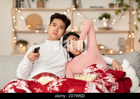 Couple chinois ennuyé regardant la télévision hurler célébrant Noël à la maison Banque D'Images