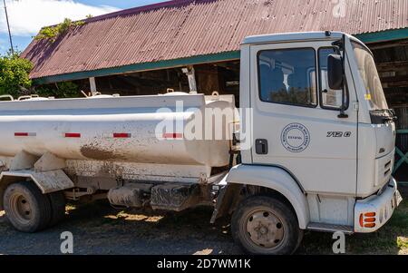 Île de Riesco, Chili - 12 décembre 2008 : propriété de camion-citerne blanc de la commune de Rio Verde garée sur terre devant une grange à toit rouge. Banque D'Images