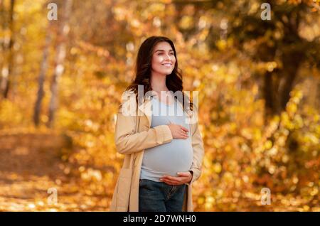 Belle femme enceinte millénaire tenant son ventre dans le parc d'automne Banque D'Images