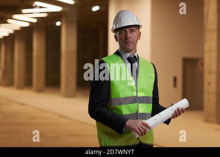 Portrait d'homme d'affaires mature portant un casque et regardant l'appareil photo lorsqu'il se trouve sur le chantier, à l'intérieur, dans l'espace de copie Banque D'Images