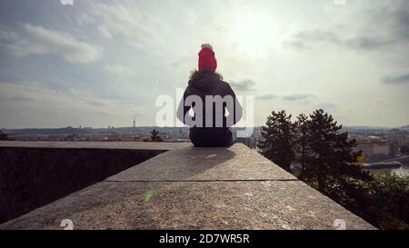 Femme en veste d'hiver assise sur un mur dans le Parc de Letna et vue sur le panorama de Prague Banque D'Images