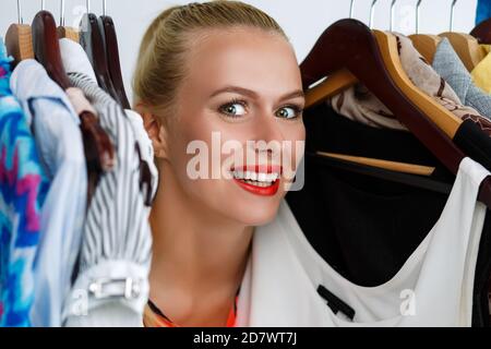 Belle femme blonde souriante debout à l'intérieur de la penderie pleine de vêtements Banque D'Images