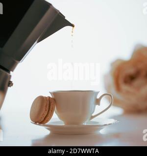 Café versé dans une tasse en porcelaine blanche avec un macaron d'une cafetière noire Banque D'Images