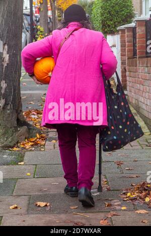 Une dame portant un rose vif porte une citrouille à la maison pour halloween Banque D'Images