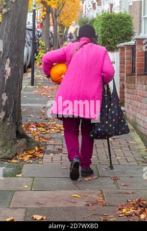 Une dame portant un rose vif porte une citrouille à la maison pour halloween Banque D'Images