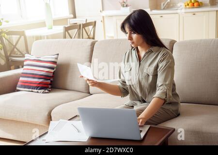 Jeune femme indienne tenant une lettre en utilisant un ordinateur portable payant la facture en ligne à la maison. Banque D'Images