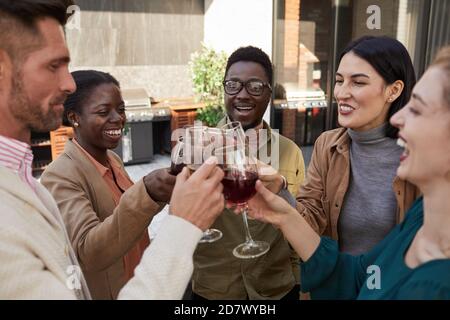 Portrait d'un groupe multiethnique d'amis qui se clinquent des lunettes tout en appréciant vin pendant la fête en plein air sur la terrasse Banque D'Images