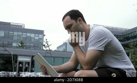 Homme sérieux et décontracté utilisant une tablette numérique assis à l'extérieur. Banque D'Images