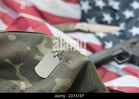 Jeton d'étiquette chien de l'armée avec balles de 9 mm et pistolet se trouve sur le drapeau américain plié et uniforme de camouflage. Un ensemble d'articles militaires vétéran américains ou de vieux devoir Banque D'Images