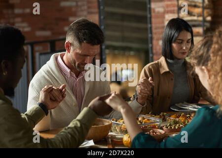 Portrait d'un homme mûr élégant qui priait et tient les mains tout en étant assis à la table du dîner pendant la célébration de Thanksgiving avec des amis et la famille, espace de copie Banque D'Images