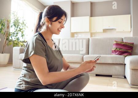 Femme indienne souriante et de grande taille utilisant une application mobile de fitness à la maison. Banque D'Images