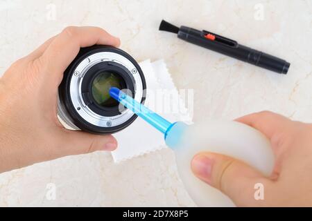 Mains soufflant de la poussière de la lentille arrière à l'aide d'un souffleur d'air en silicone. Élimination régulière de la poussière et des taches des équipements photographiques. Gros plan sur l'entretien. Banque D'Images