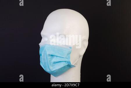 Buste blanc de mannequin avec masque hygiénique bleu sur noir arrière-plan Banque D'Images